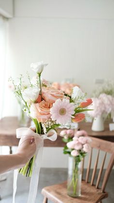 a person holding a bouquet of flowers in front of a table with two wooden chairs