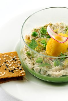 a bowl of food on a plate next to a cracker and some sort of appetizer