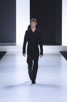 a man walking down a runway in a black shirt and pants with his hands on his hips