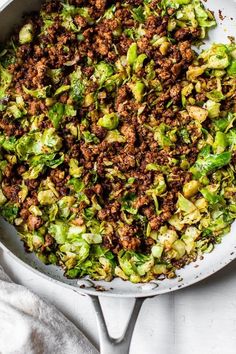 a skillet filled with chopped brussels sprouts and ground beef, on top of a white cloth