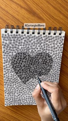 someone is drawing a heart on a spiral bound notebook with black and white dots, while holding a marker