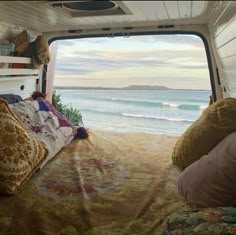 the inside of a camper with a bed and pillows on it, looking out at the ocean