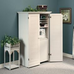 a white cabinet sitting in the corner of a room next to a potted plant