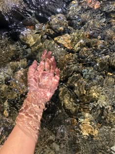 a person's hand in the water with rocks and stones around them, as if they were reaching for something