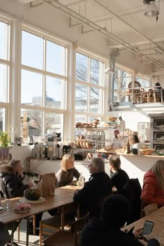 several people sitting at tables in a large room with big windows looking out onto the street