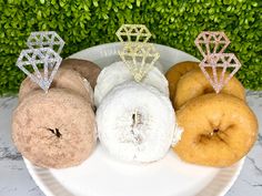 four donuts and three diamond shaped rings on a white plate with greenery in the background