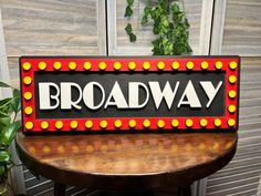 a broadway sign sitting on top of a wooden table next to a potted plant