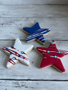 three decorated cookies in the shape of stars on a white wooden surface with red, white and blue icing