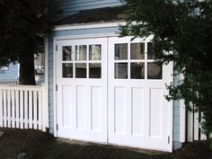 an image of a white garage door in front of a blue house with trees on the side