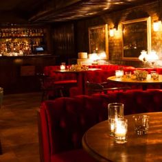 a dimly lit restaurant with red velvet chairs and wooden tables in front of the bar