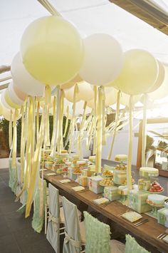 a table topped with lots of white balloons and cake on top of wooden tables covered in green napkins