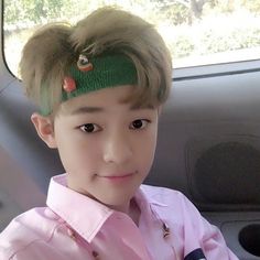 a young boy wearing a pink shirt and green headband in the back seat of a car