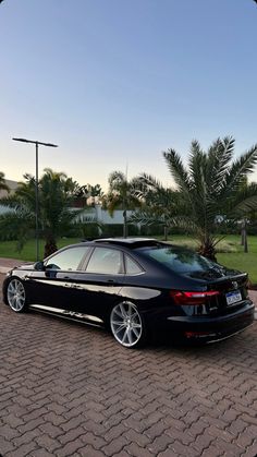 a black car parked on the side of a brick road next to a palm tree