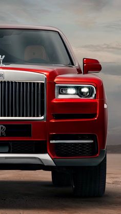 the front end of a red rolls royce parked on top of a sandy beach with dark clouds in the background