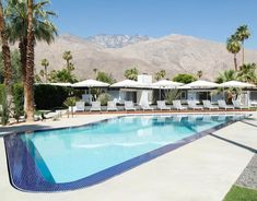 an empty swimming pool with lounge chairs and palm trees in the foreground, surrounded by mountains