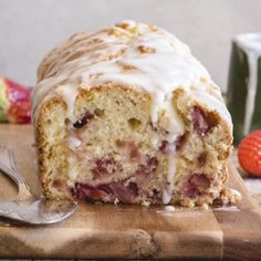 a loaf of cake sitting on top of a cutting board next to some strawberries