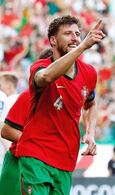 a male soccer player in a red shirt and green shorts with his hand out to the side