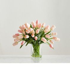 a vase filled with pink tulips sitting on top of a table next to a white wall