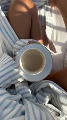 a woman laying in bed with a cup of coffee on her lap and blanket over her