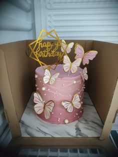 a pink birthday cake with butterflies on it in a cardboard box that says happy birthday