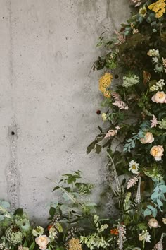 an arrangement of flowers and greenery against a concrete wall