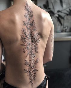 the back of a woman's body with tattoos on it and flowers in the center