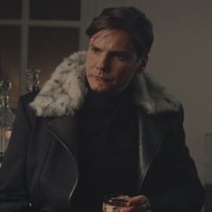 a man in a fur collar holding a drink