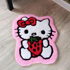 a hello kitty rug on the floor with a strawberry in its mouth and a bow