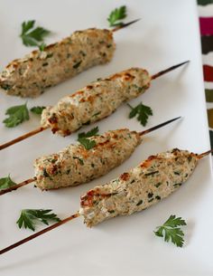 four chicken skewers with parsley on them are sitting on a white plate