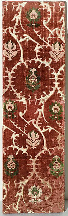 an old red rug with green and white designs on the bottom, in front of a white wall