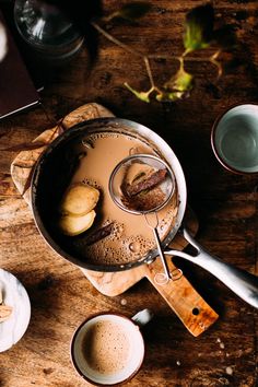 a wooden table topped with cups and saucers filled with liquid next to an open book