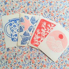 three cards with different designs on them sitting on a floral tablecloth, one is red and the other is blue