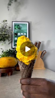 a person holding an ice cream cone with yellow flowers in it on top of a table