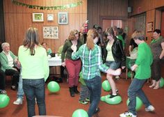 a group of people standing around each other in a room with green balloons on the floor