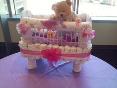 a teddy bear sitting in a crib on top of a purple table cloth covered table