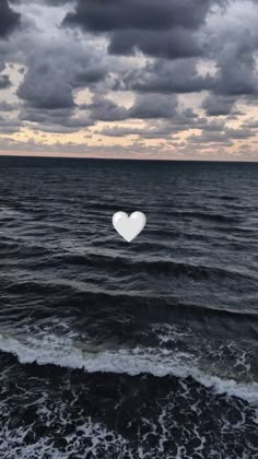 a white heart floating in the middle of an ocean with dark clouds above and water below