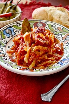 a plate filled with pasta and meat on top of a red table cloth next to bread