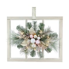 a christmas wreath hanging on the side of a window with pine branches and ornaments in it