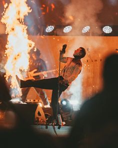 a man standing on top of a metal pole in front of a fire filled stage