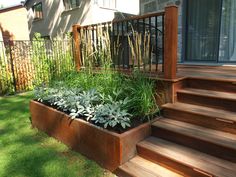 a wooden planter filled with lots of plants on top of grass next to stairs