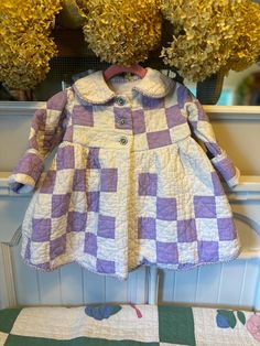 a purple and white checkered coat sitting on top of a bed next to flowers