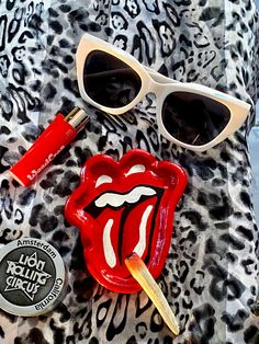 a pair of sunglasses and lipstick on top of a leopard print blanket with the rolling stones logo