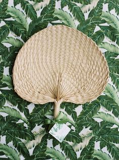 a woven wicker umbrella on a green and white tropical print wallpaper with palm leaves