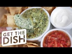 a hand holding a tortilla chip over a tray of chips and dips