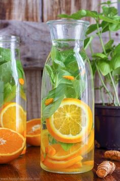 two glass vases filled with orange slices and greens on top of a wooden table