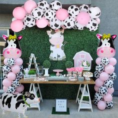 a table topped with balloons and cow figurines next to a wall covered in fake grass