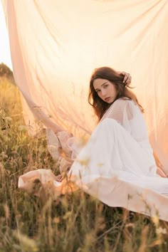 a woman is sitting in the grass with her arms around her head and wearing a white dress