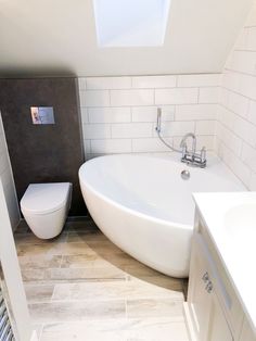 a white bath tub sitting next to a toilet in a bathroom under a skylight