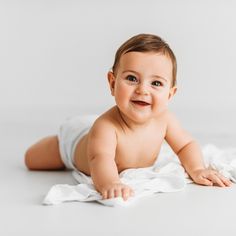 a baby laying on its back in a diaper and looking at the camera while smiling