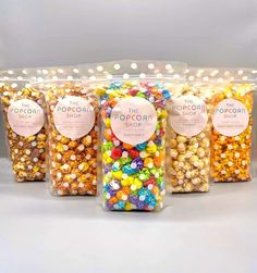 four bags of popcorn with different colored candies in them, all lined up and labeled the popcorn shop